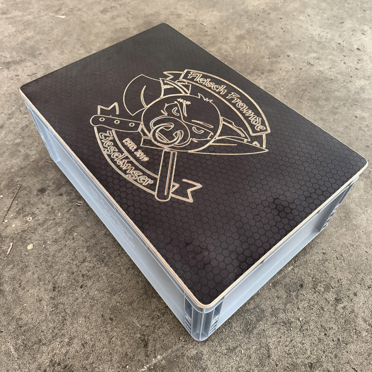 Eurobox-Deckel Hexagon 600 × 400 mm mit eingefrästem Vereinslogo, liegend auf einer grauen Eurobox